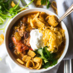 vegetarian chili in a bowl on a white background with sour cream, cheese, and Fritos