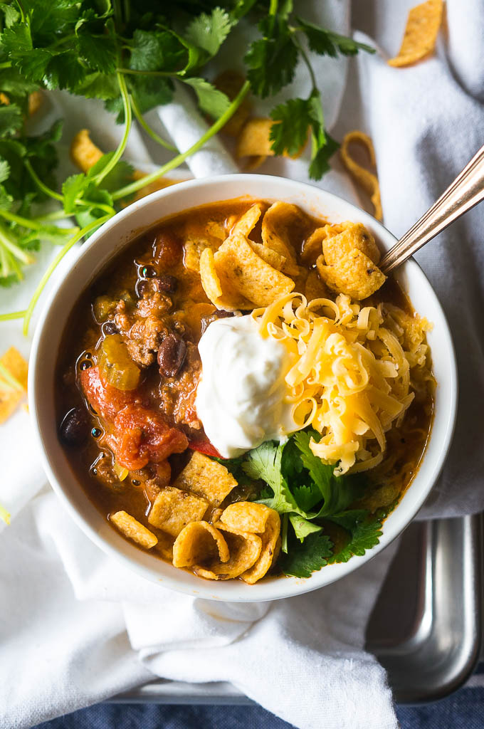 vegetarian chili in a bowl on a white background with sour cream, cheese, and Fritos