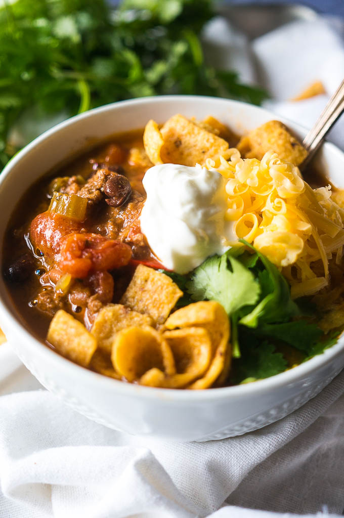 vegetarian chili in a bowl on a white background with sour cream, cheese, and Fritos