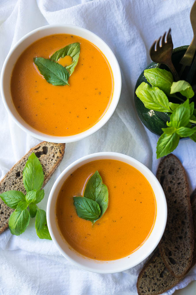 Creamy Tomato Basil Soup topped with basil in a white bowl on a white napkin, served with bread. 