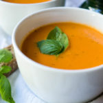 Tomato soup in a white bowl with basil leaves