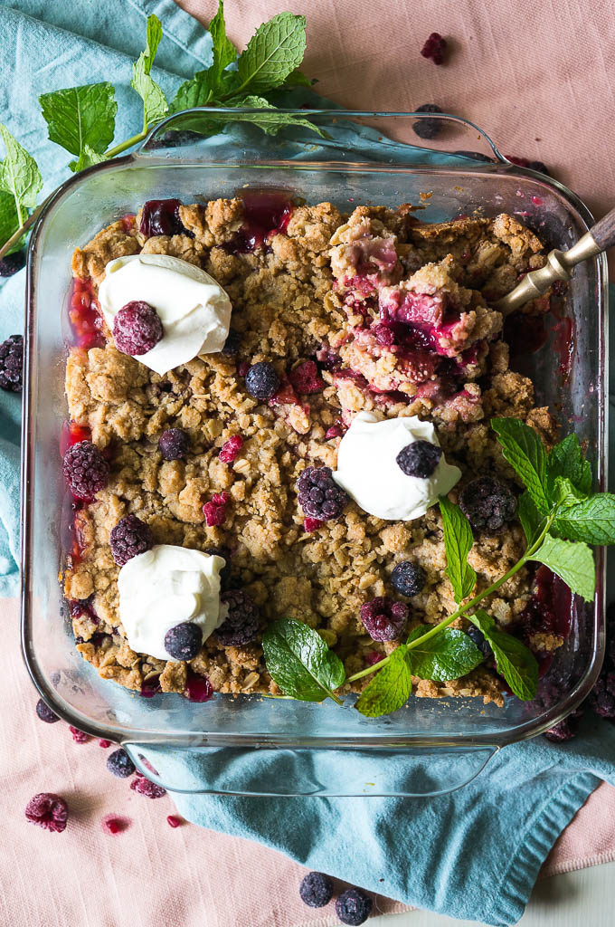 Berry Rhubarb Crisp with whipped topping, mint sprig, on a blue and pink napkin.