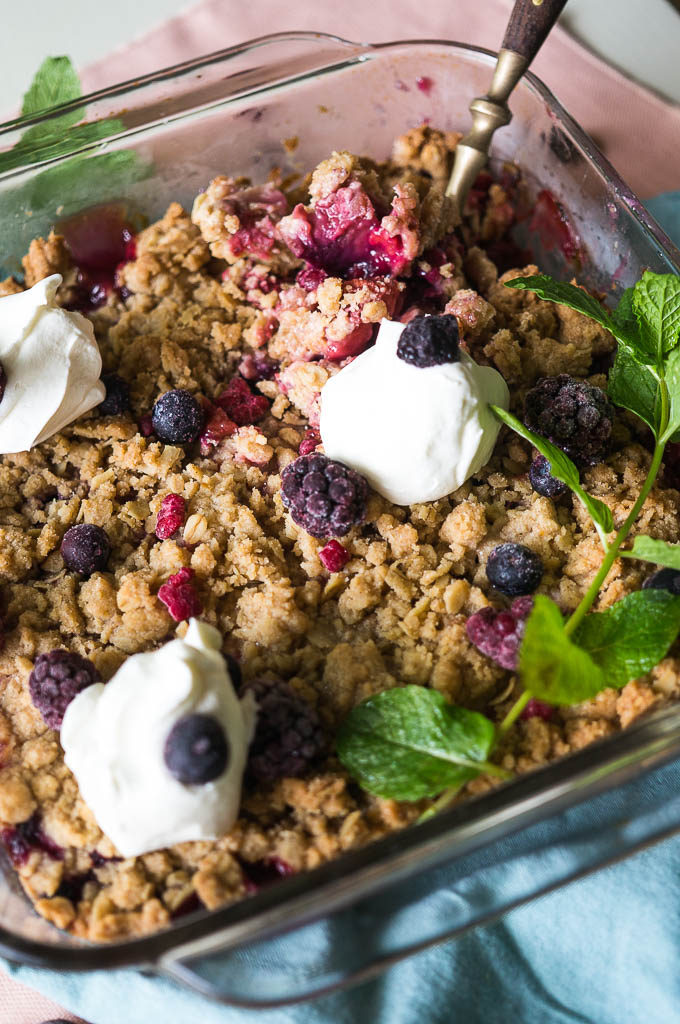 Berry Rhubarb Crisp with whipped topping, mint sprig, on a blue and pink napkin.