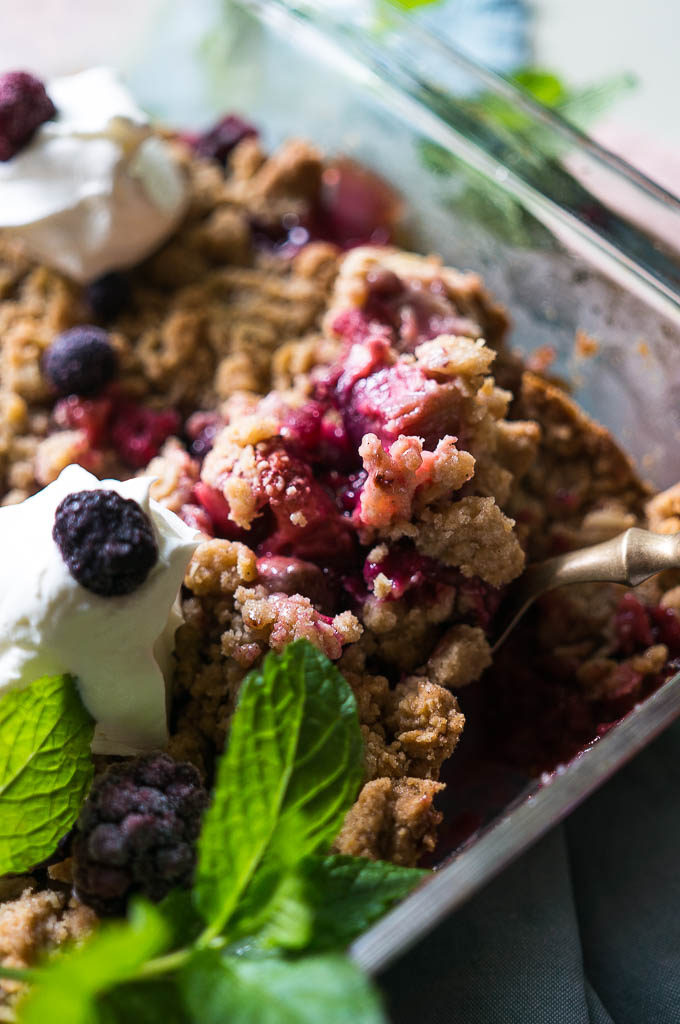Berry Rhubarb Crisp with whipped topping, mint sprig, on a blue and pink napkin.
