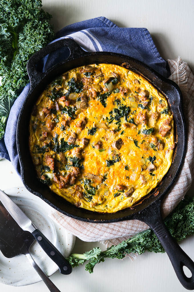 Eggs, Sausage, and Mushrooms in a cast iron skillet on a white background with kale and napkins.