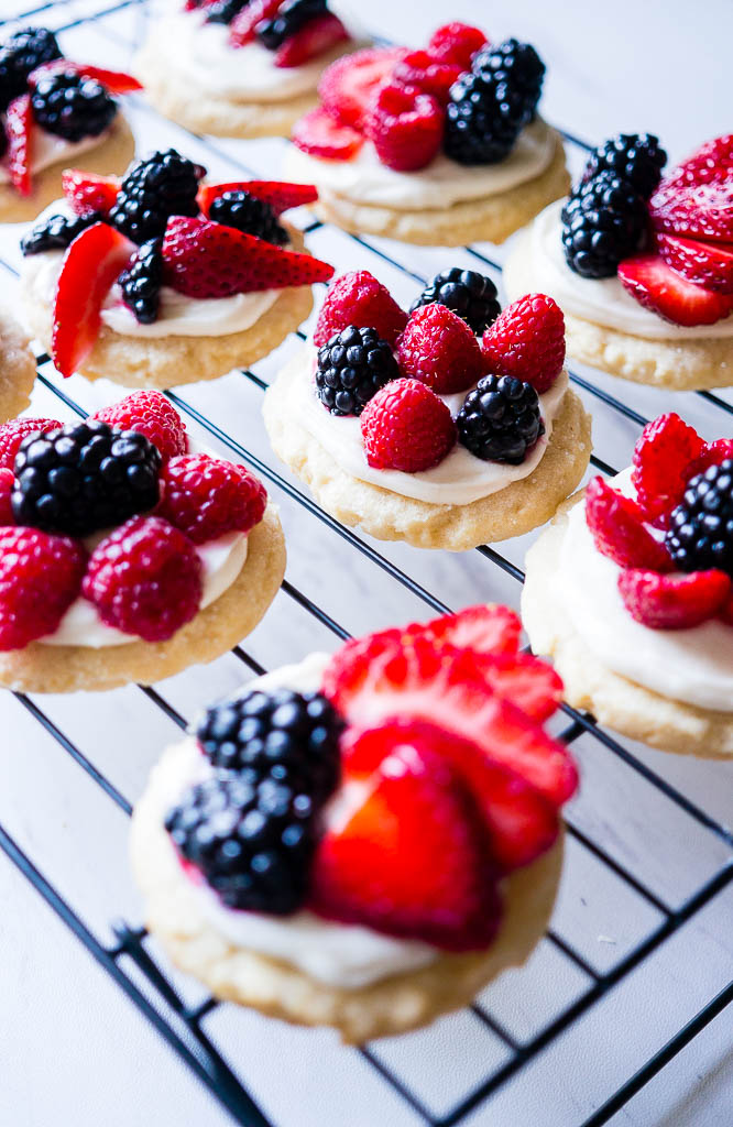 Patriotic Mini Fruit Pizzas.  A fun dessert for 4th of July with a classic sugar cookie base, a scrumptious cream cheese frosting, and your choice of red and blue fruit!