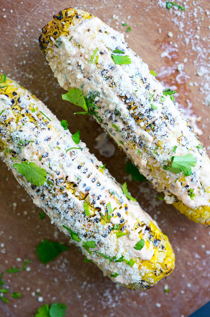 Grilled Mexican Street Corn is lathered in a spicy mayo and sour cream mixture, then sprinkled with cilantro and parmesan cheese.