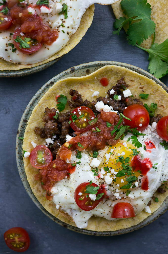 Huevos Rancheros Breakfast Tacos are loaded with sausage, beautiful ripe cherry tomatoes, a sunny side up runny egg, and a hot sauce kind of kick in the pants.