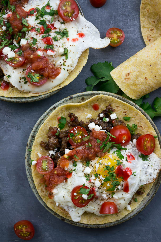 Huevos Rancheros Breakfast Tacos are loaded with sausage, beautiful ripe cherry tomatoes, a sunny side up runny egg, and a hot sauce kind of kick in the pants.
