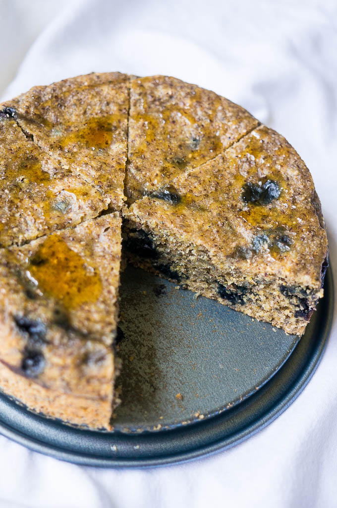 Blueberry Cornmeal Breakfast Cake on a black springform pan, drizzled with honey, and a white background.