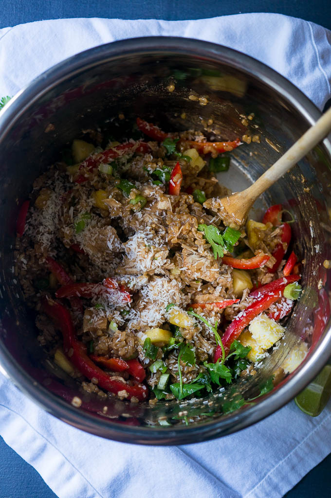 Caribbean Chicken and rice, red peppers, pineapple, and cilantro cooking in the instant pot bowl with a wooden spoon on a white napkin.