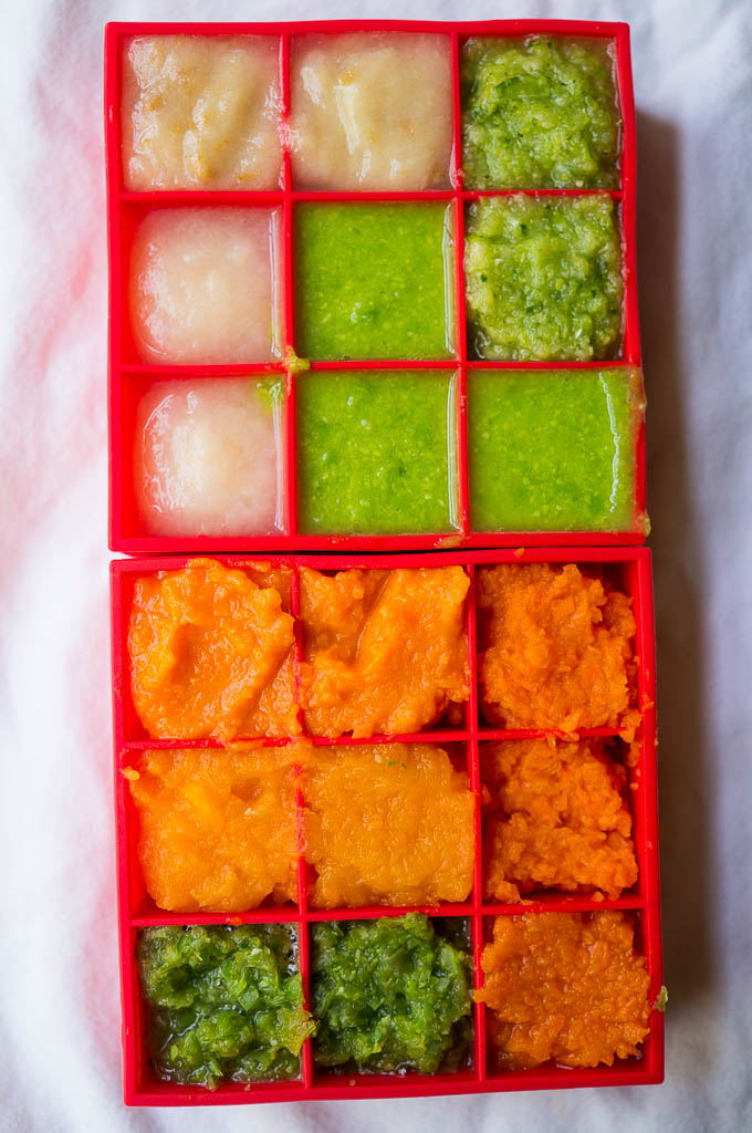 Puree'd baby food in a red silicone freezer tray on a white background.