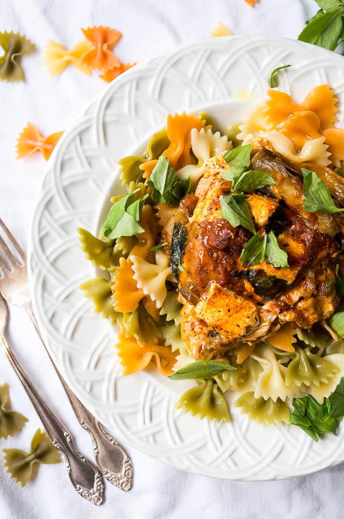 chicken and eggplant pasta in a wide white bowl sprinkled with fresh basil.