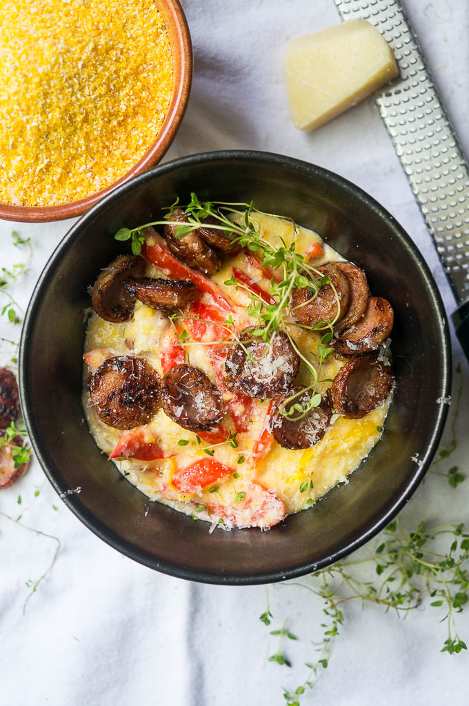 Sausage, polenta, thyme in a black bowl on a white background.