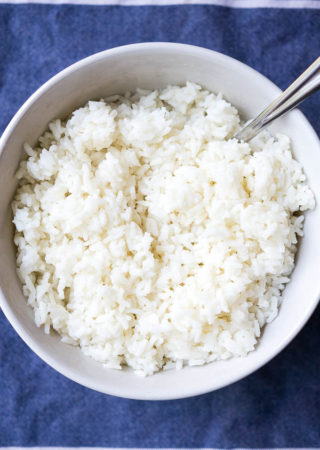 Fluffy white basmati rice in a white bowl on a blue background.