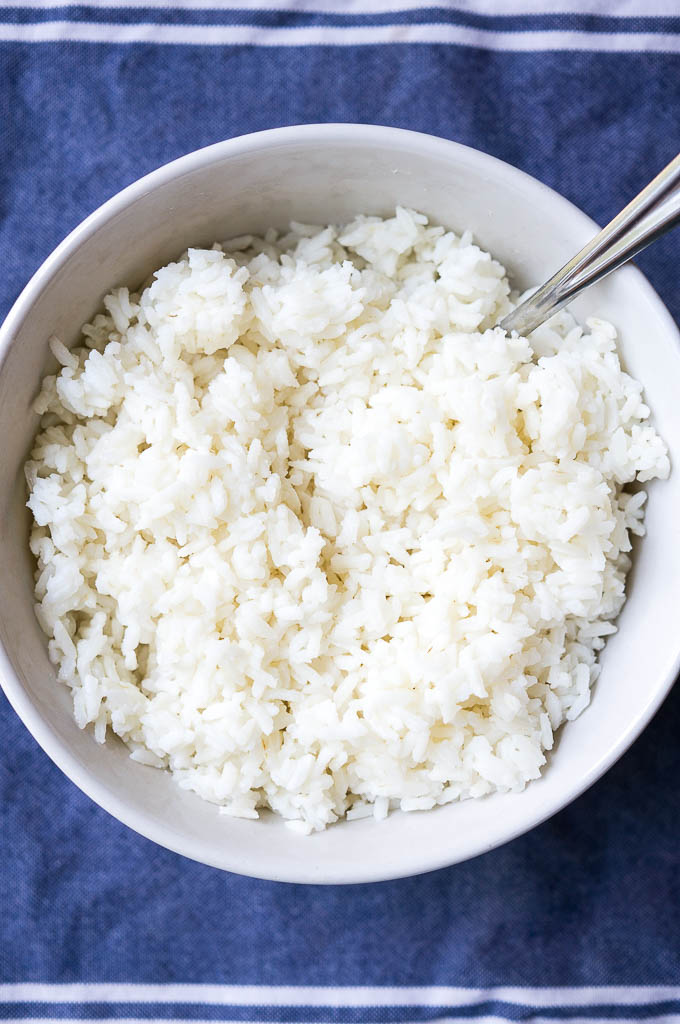 White Basmati Rice in a white bowl with a silver spoon on a blue napkin.