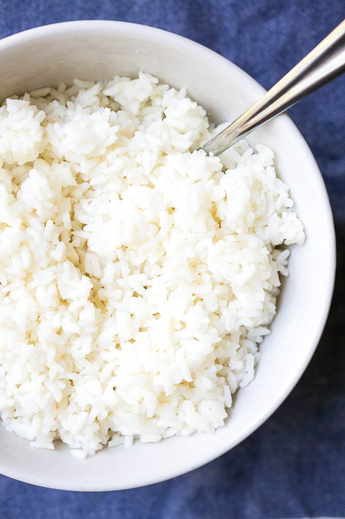 White Basmati Rice in a white bowl with a silver spoon on a blue napkin.