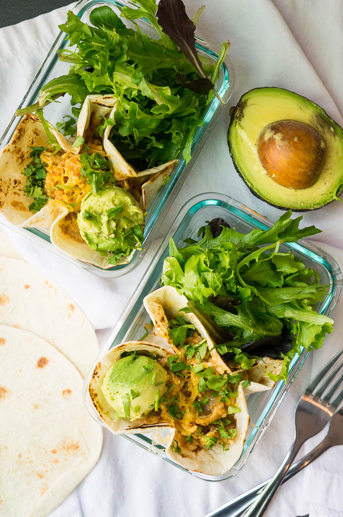 Chicken and Rice Burrito Bowls with lettuce and avocado in a glass container on a white napkin, served with avocado and tortillas.