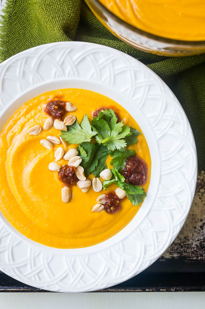 Gingery carrot soup in a white bowl, topped with cilantro, red chili paste, and chopped peanuts on a green napkin.