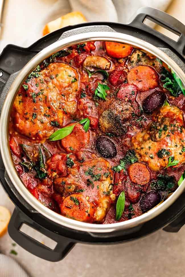 Instant pot chicken cacciatore with tomatoes, bell peppers, kale, carrots, and mushrooms in the instant pot on a brown table.