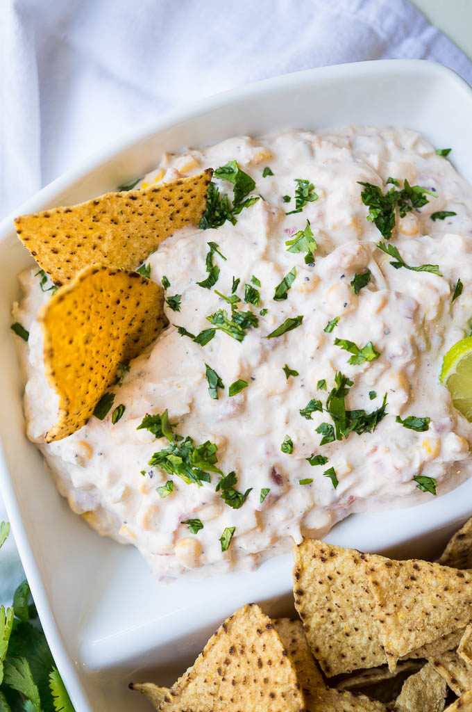 Creamy chicken and cheese dip with tortilla chips in a white dish.