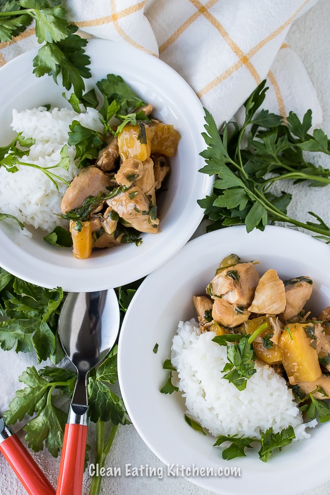 Instant pot teriyaki chicken served over white rice in a white bowl, garnished with parsley with an orange and white checkered napkin and a red and silver spoon.