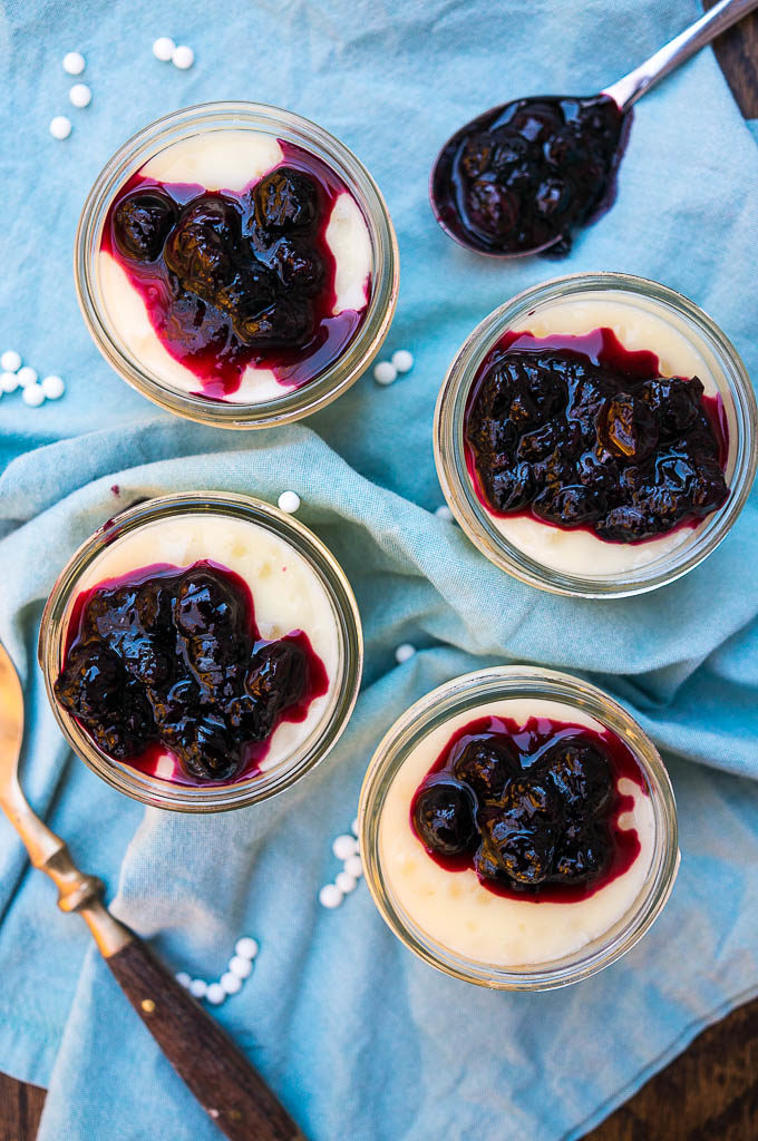 Pudding in glass containers with blueberry sauce on a blue napkin.