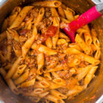 Penne pasta in red sauce with sausage in a metal pot.