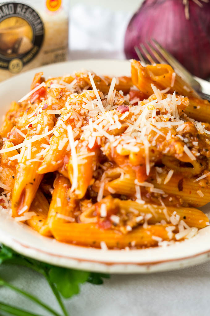 Penne pasta in red sauce with sausage and parmesan cheese on a white plate.