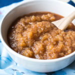 Chunky applesauce in a white bowl on a blue napkin with a wooden spoon.