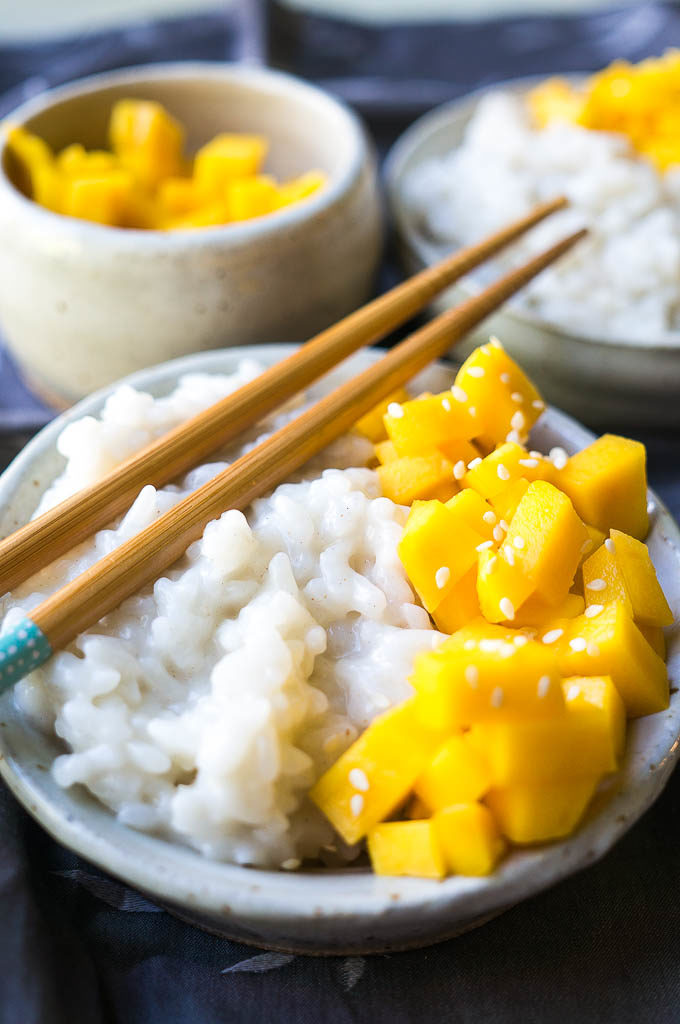 Mango, white rice, and sesame seeds on a white plate on a gray background.