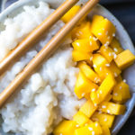 Mango, white rice, and sesame seeds on a white plate on a gray background.